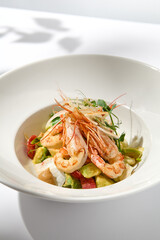 Elegant food - salad with shrimp and avocado on white table with harsh shadow. Flashy food concept. Seafood salad with shrimp, tomatoes and avocado on white plate with sunlight.