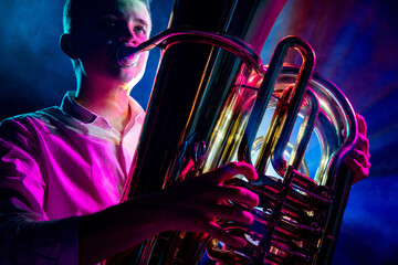Detailed photo of tuba being played by artistic musician, highlighted by glow of dramatic stage lighting. Concept of art, hobby and work, music festivals, concerts, symphony show, culture.