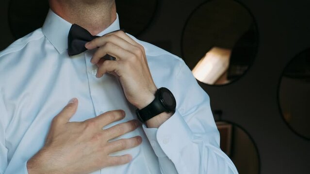 a man in a white shirt adjusts a black bowtie