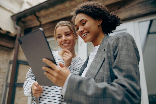Smiling female business people standing at office terrace and using digital tablet together