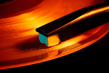Close-up photo of turntable needle on vinyl record with warm orange glow. Vinyl record player,...