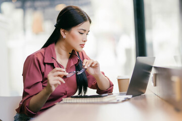 A woman wearing glasses is sitting at a table with a laptop and a cup of coffee