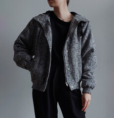 Woman wearing grey bomber jacket and black trousers isolated on light background.