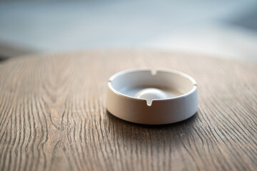 An empty white ceramic ashtray or cigarette butt tray is placed on wooden table.