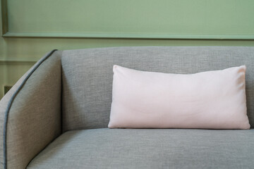 Square white pillow placed on grey sofa at the hotel lobby room. Interior decoration and furniture object photo, close-up.