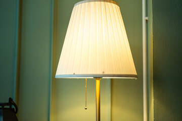 A luxury electric lighting lamp with golden metal part and chain pulling switch, it glowing in warmlight shade. Interior decoration object photo, close-up and selective focus at the lamp part.