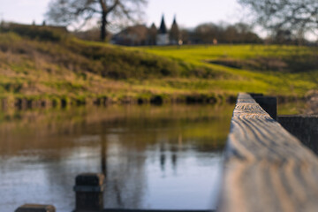 Spring landscape with tree and river, Oast houses in background. Depth of field view to wooden barrier fence.