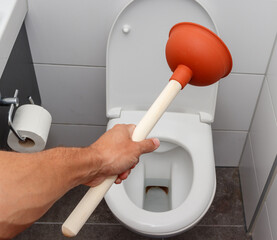 Young man using plunger to unclog a toilet bowl