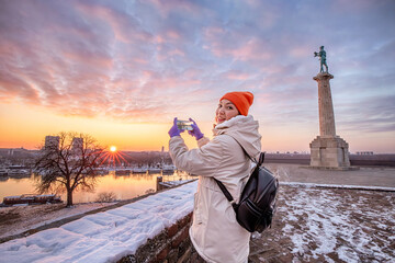 In the heart of Belgrade's Kalemegdan, a young woman taking smartphone photo and captures the city's scenic sunset panorama - 776144879