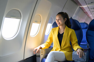 A woman in a yellow jacket sits in an airplane seat with her arms crossed