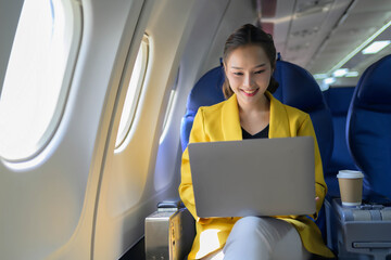 A woman is sitting on an airplane with a laptop open in front of her