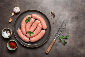 Fresh raw sausages with spices on a dark grunge background. Top view, flat lay, copy space.