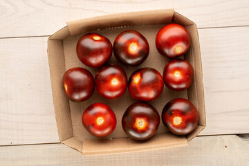 Several juicy black cherry tomatoes in a paper plate on a wooden table, macro, top view.