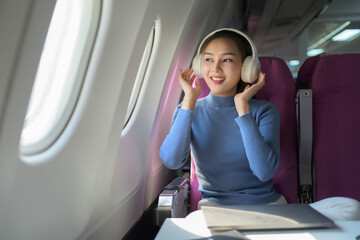 A woman wearing headphones is sitting in an airplane seat