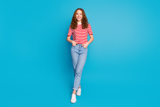 Full size photo of cool gorgeous girl wear stylish t-shirt denim trousers holding arms in pockets isolated on blue color background
