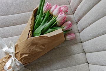 Bouquet of fresh pastel pink tulips wrapped in the craft paper decorated with satin ribbon