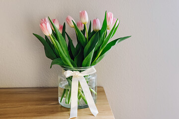 Bouquet of fresh pastel pink tulips in a glass vase decorated with satin ribbon