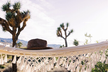Hat lying on the hammock with Joshua trees on the background, boho lifestyle