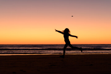 woman silhouette jumping in the beach before sunrise - obrazy, fototapety, plakaty