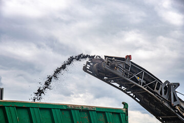 Slag dumping belt of grader on a road resurfacing repairs, removing asphalt and loading it into the...