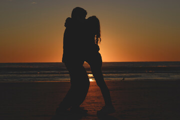 young couple silhouette at the beach hugging during sunrise