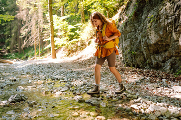 Hiking in nature. Young woman with a yellow backpack  walks along a hiking trail against the backdrop of mountain scenery. Adventure, travel, tourism.