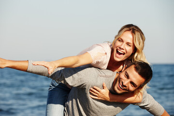 Couple, flying and piggyback on vacation, smile and peace at beach or game by blue sky. People, happy and tropical island for bonding on weekend, outdoor nature and love for marriage or romance