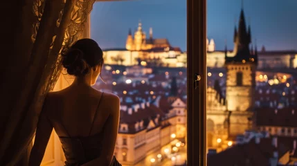 Foto op Plexiglas anti-reflex A graceful lady standing by a large window with a view of historic buildings in the city of Prague, Czech Republic in Europe. © rabbit75_fot