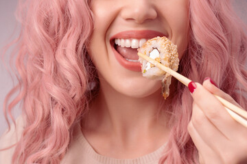 Young woman with red nails and pink hair is eating sushi.