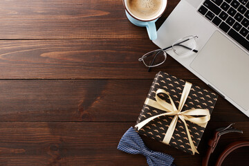 Father's workday tribute: Overhead view of a professional's desk with laptop, coffee, glasses, and a festive gift, celebrating Father's Day at the workplace