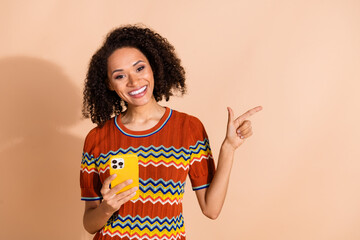 Photo of cheerful gorgeous woman wear knit t-shirt hold smartphone indicating at logo empty space...