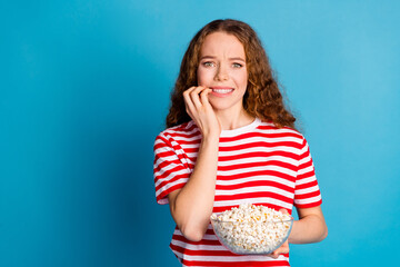 Portrait of worried astonished girl wear stylish t-shirt hold popcorn biting fingers staring at...