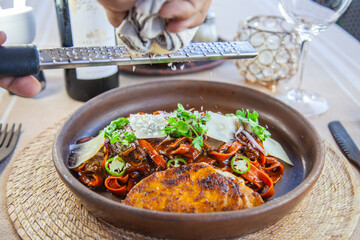 Pasta fresca hecha en casa teñida con puré de mix de chiles secos , con birria típica de Jalisco, acompañada de quesabirria, cebolla caramelizada, cilantro, chile serrano y queso nacional añejado