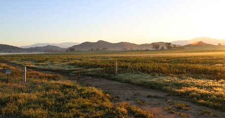 Beautiful country rural field landscape with sun rising and mountains in background looking at gate entrance