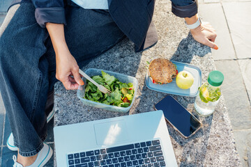 Top view business woman having lunch break, eating fast and healthy in front of laptop outdoors....