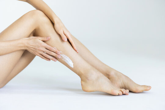 Woman applying body cream onto her smooth legs on light grey background