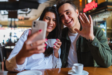 A young couple boyfriend and girlfriend or friends are drinking coffee having fun and taking selfies in cafe or restaurant 