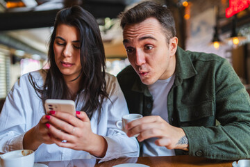 A young couple boyfriend and girlfriend or friends are drinking coffee having fun and taking selfies in cafe or restaurant