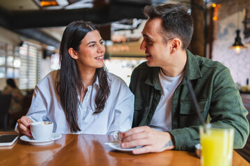 A young couple boyfriend and girlfriend or friends are drinking coffee having fun and taking selfies in cafe or restaurant 