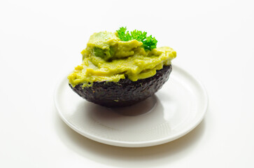 A green avocado with parsley on top sits on a white plate - 776207618
