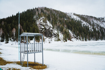 Snowcovered lifeguard tower on shore of freezing lake in mountainous landscape