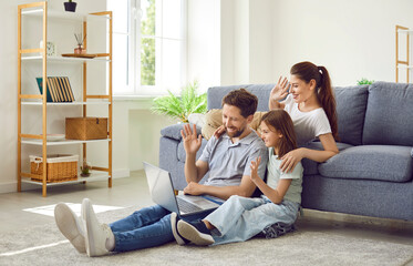 Happy family using laptop and video calling relatives. Young mother, father and child daughter sitting in living room at home, looking at screen of modern notebook computer, waving hello and smiling - obrazy, fototapety, plakaty