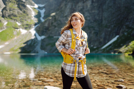 Young woman with a yellow hiking backpack traveling along hiking trails in the mountains among forests and cliffs.  Lifestyle, adventure, nature, active life.