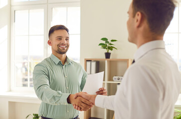 Happy smiling man shaking hands with his partner standing in office celebrating success or making a...