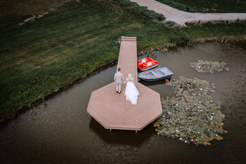 Valmiera, Latvia - Augist 13, 2023 - A bride and groom walk on a narrow pier leading to an...