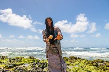 an African American woman wearing sunglasses with long sister locks relaxing at Sandy Beach with blue ocean water, crashing waves blue sky and clouds in Honolulu Hawaii