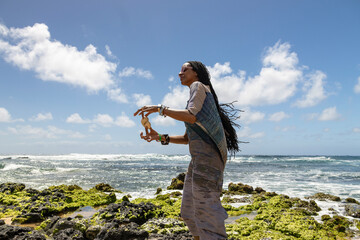 an African American woman wearing sunglasses with long sister locks relaxing at Sandy Beach with blue ocean water, crashing waves blue sky and clouds in Honolulu Hawaii
