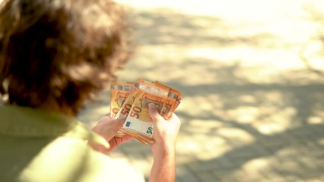 Young man counting money outside on a sunny day