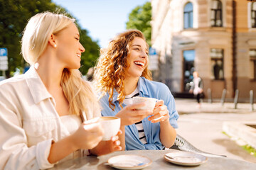 Portrait of a smiling young women friends sitting outdoors in cafe drinking coffee. Fashion, beauty, relax, tourism.