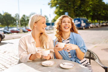 Portrait of a smiling young women friends sitting outdoors in cafe drinking coffee. Fashion, beauty, relax, tourism.